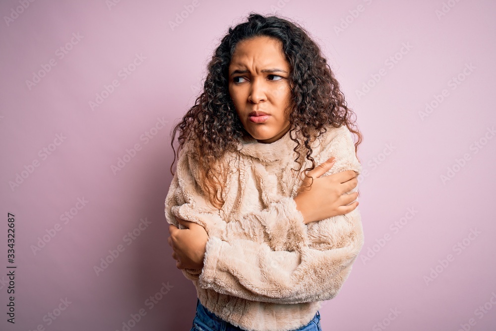 Young beautiful woman with curly hair wearing casual sweater standing over pink background shaking and freezing for winter cold with sad and shock expression on face Young beautiful woman with curly hair wearing casual sweater standing over pink background shaking and freezing for winter cold with sad and shock expression on face