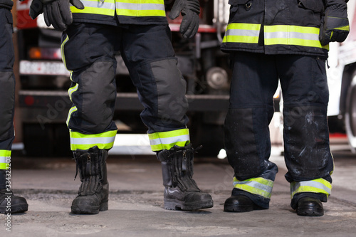 Abstract professional firefighters wearing uniforms and protective helmets. Firetruck in the background.