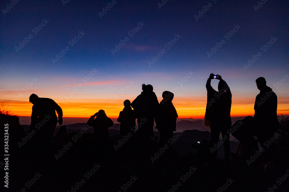 Joven y grupo de personas tomando foto con celular al amanecer en la montaña Joven y grupo de personas tomando foto con celular al amanecer en la montaña