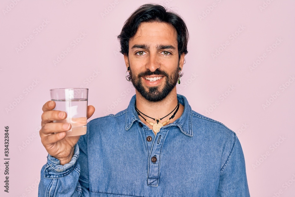 Young handsome hispanic bohemian hipster man with bear drinking a fresh glass of water with a happy face standing and smiling with a confident smile showing teeth Young handsome hispanic bohemian hipster man with bear drinking a fresh glass of water with a happy face standing and smiling with a confident smile showing teeth