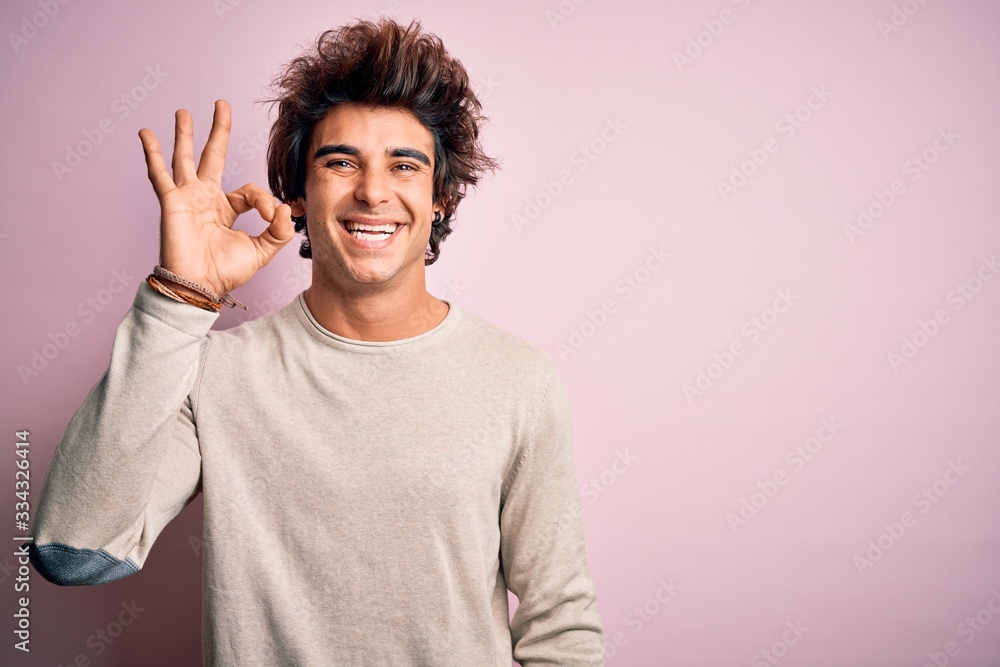 Young handsome man wearing casual t-shirt standing over isolated pink background smiling positive doing ok sign with hand and fingers. Successful expression. Young handsome man wearing casual t-shirt standing over isolated pink background smiling positive doing ok sign with hand and fingers. Successful expression.