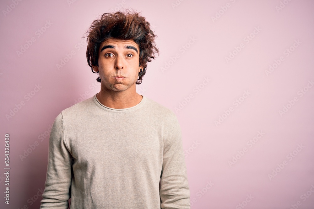 Obraz premium Young handsome man wearing casual t-shirt standing over isolated pink background puffing cheeks with funny face. Mouth inflated with air, crazy expression.