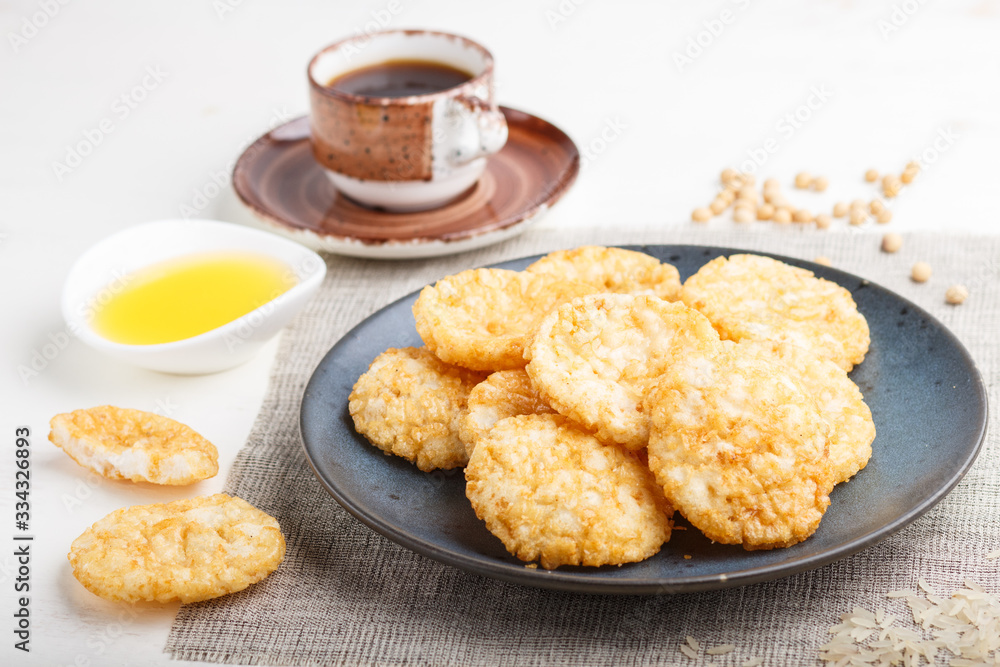Traditional japanese rice chips cookies with honey and soy sauce on a blue ceramic plate and a cup of coffee on a white wooden background. side view, selective focus. Traditional japanese rice chips cookies with honey and soy sauce on a blue ceramic plate and a cup of coffee on a white wooden background. side view, selective focus.