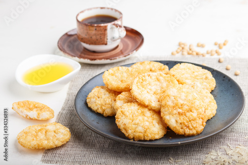 Traditional japanese rice chips cookies with honey and soy sauce on a blue ceramic plate and a cup of coffee on a white wooden background. side view  selective focus.