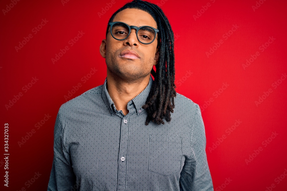 Fototapeta premium Young handsome african american man with dreadlocks wearing casual shirt and glasses Relaxed with serious expression on face. Simple and natural looking at the camera.