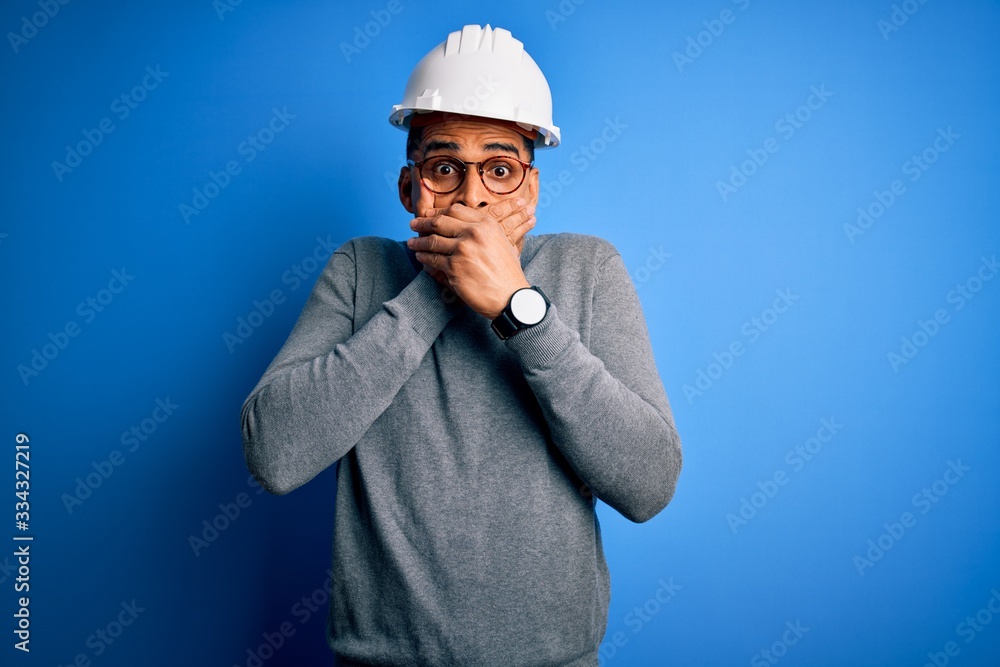 Young handsome african american engineer man with dreadlocks wearing safety helmet shocked covering mouth with hands for mistake. Secret concept. Young handsome african american engineer man with dreadlocks wearing safety helmet shocked covering mouth with hands for mistake. Secret concept.