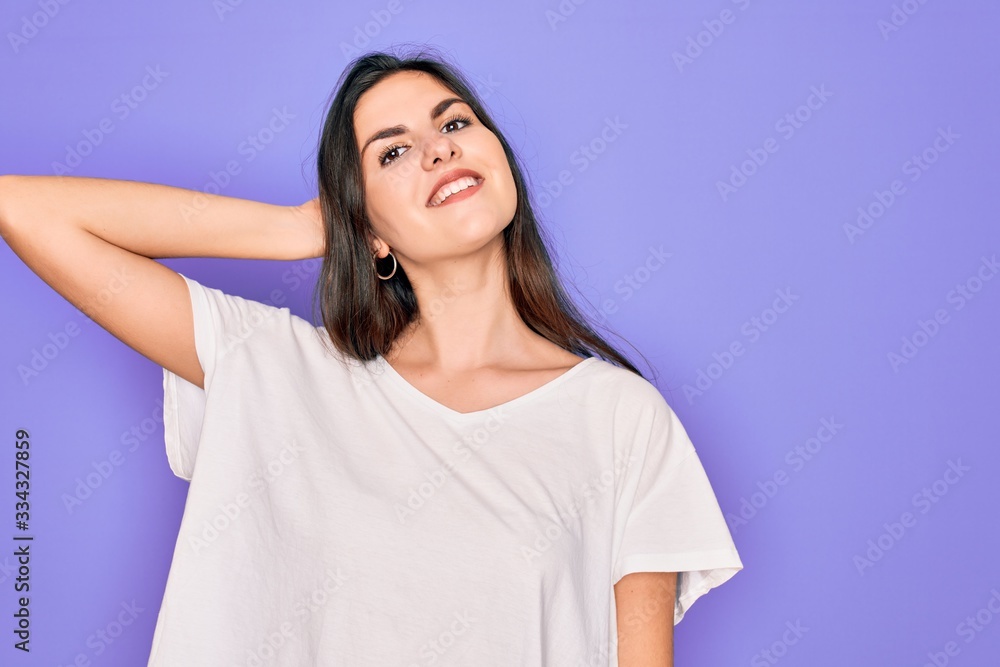 Obraz premium Young beautiful brunette woman wearing casual white t-shirt over purple background smiling confident touching hair with hand up gesture, posing attractive and fashionable