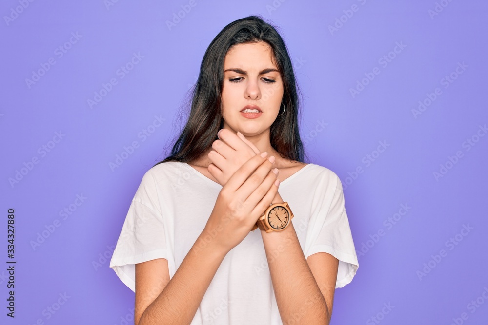 Young beautiful brunette woman wearing casual white t-shirt over purple background Suffering pain on hands and fingers, arthritis inflammation Young beautiful brunette woman wearing casual white t-shirt over purple background Suffering pain on hands and fingers, arthritis inflammation
