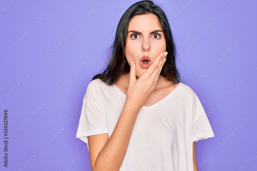 Young beautiful brunette woman wearing casual white t-shirt over purple background Looking fascinated with disbelief, surprise and amazed expression with hands on chin Young beautiful brunette woman wearing casual white t-shirt over purple background Looking fascinated with disbelief, surprise and amazed expression with hands on chin