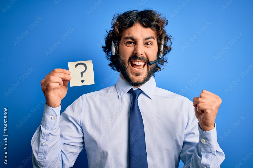 Young call center agent man with beard working using headset holding question mark reminder screaming proud and celebrating victory and success very excited, cheering emotion Young call center agent man with beard working using headset holding question mark reminder screaming proud and celebrating victory and success very excited, cheering emotion