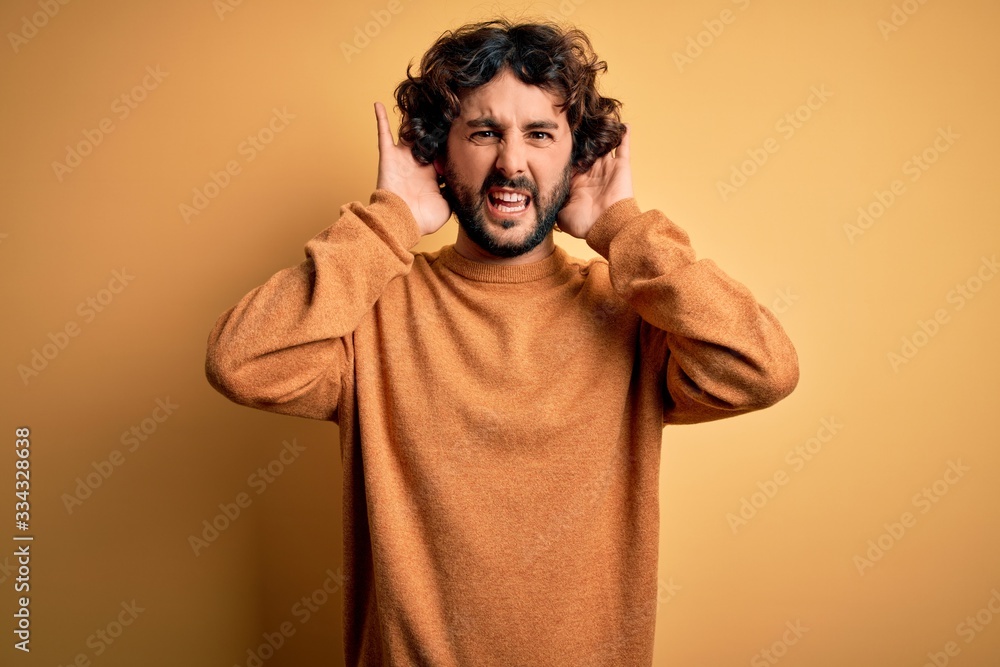Young handsome man with beard wearing casual sweater standing over yellow background Trying to hear both hands on ear gesture, curious for gossip. Hearing problem, deaf Young handsome man with beard wearing casual sweater standing over yellow background Trying to hear both hands on ear gesture, curious for gossip. Hearing problem, deaf