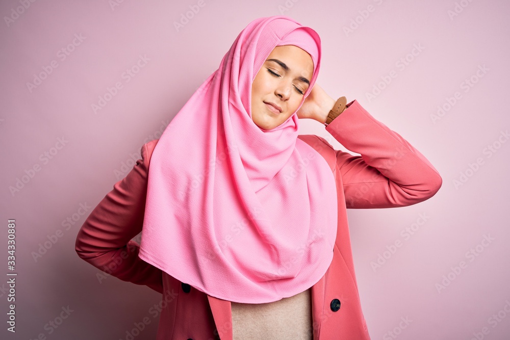 Young beautiful girl wearing muslim hijab standing over isolated pink background Suffering of neck ache injury, touching neck with hand, muscular pain Young beautiful girl wearing muslim hijab standing over isolated pink background Suffering of neck ache injury, touching neck with hand, muscular pain