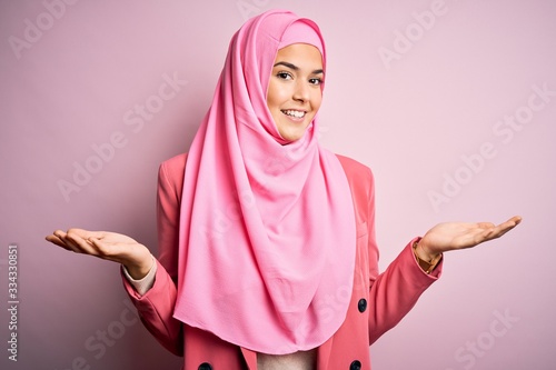 Young beautiful girl wearing muslim hijab standing over isolated pink background smiling showing both hands open palms, presenting and advertising comparison and balance