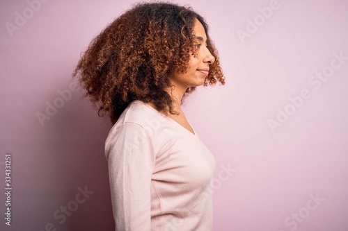 Young african american woman with afro hair wearing casual sweater over pink background looking to side  relax profile pose with natural face with confident smile.