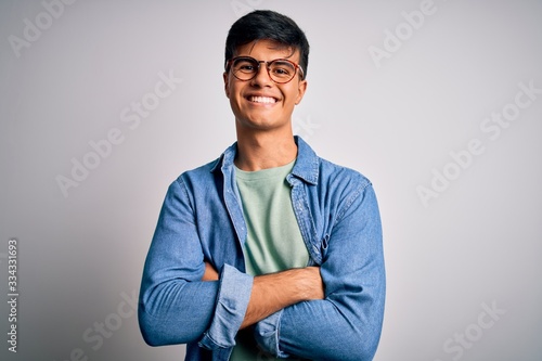 Young handsome man wearing casual shirt and glasses over isolated white background happy face smiling with crossed arms looking at the camera. Positive person.