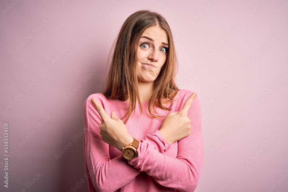 Young beautiful redhead woman wearing casual sweater over isolated pink background Pointing to both sides with fingers, different direction disagree Young beautiful redhead woman wearing casual sweater over isolated pink background Pointing to both sides with fingers, different direction disagree