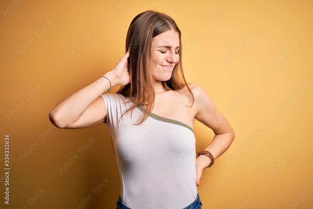 Young beautiful redhead woman wearing casual t-shirt over isolated yellow background Suffering of neck ache injury, touching neck with hand, muscular pain Young beautiful redhead woman wearing casual t-shirt over isolated yellow background Suffering of neck ache injury, touching neck with hand, muscular pain