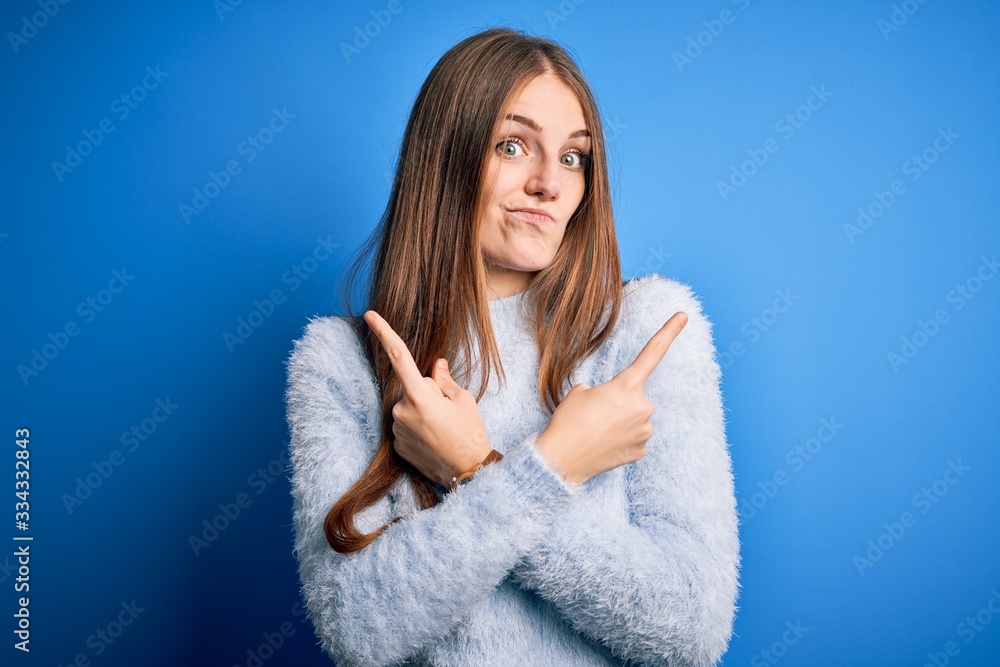 Young beautiful redhead woman wearing casual sweater over isolated blue background Pointing to both sides with fingers, different direction disagree Young beautiful redhead woman wearing casual sweater over isolated blue background Pointing to both sides with fingers, different direction disagree