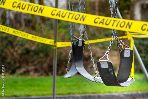 Black rubber swings in closed public playground surrounded by yellow caution tape during Corvid-19 Coronavirus pandemic photo