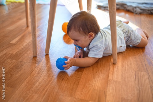 Adorable toddler sitting on the floor using pacifier around lots of toys at kindergarten