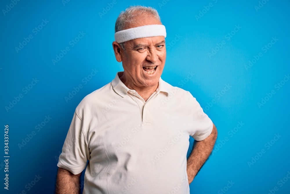 Middle age hoary sportsman doing sport wearing sportswear over isolated blue background winking looking at the camera with sexy expression, cheerful and happy face. Middle age hoary sportsman doing sport wearing sportswear over isolated blue background winking looking at the camera with sexy expression, cheerful and happy face.
