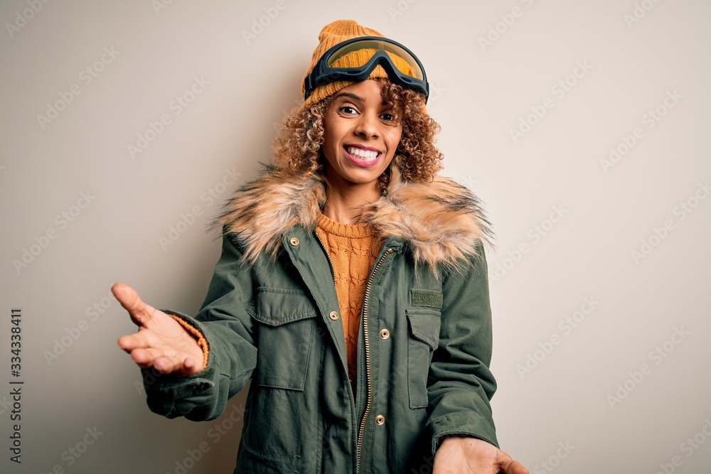Young african american skier woman with curly hair wearing snow sportswear and ski goggles smiling cheerful with open arms as friendly welcome, positive and confident greetings Young african american skier woman with curly hair wearing snow sportswear and ski goggles smiling cheerful with open arms as friendly welcome, positive and confident greetings