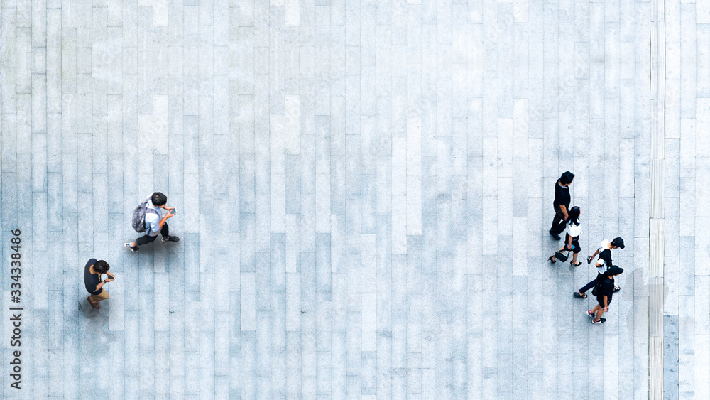 Obraz premium Human life in Social distance. Aerial top view with blur man with smartphone and group of people walking at pedestrian crosswalk on grey pavement street road with empty space.