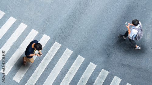 Human life in Social distance. Aerial top view with blur man with smartphone walking converse of other people at pedestrian crosswalk on grey pavement street road with empty space.