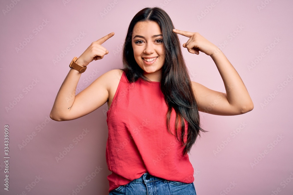 Young brunette woman wearing casual summer shirt over pink isolated background smiling pointing to head with both hands finger, great idea or thought, good memory Young brunette woman wearing casual summer shirt over pink isolated background smiling pointing to head with both hands finger, great idea or thought, good memory