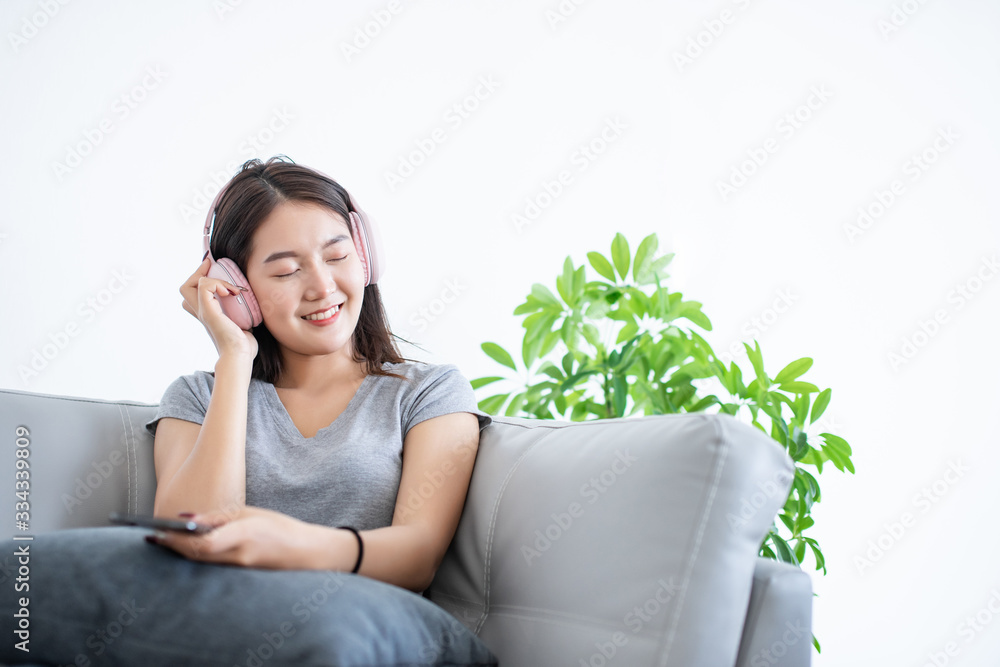 Attractive Asian young woman happy and smile for listen song from music streaming application mobile phone connect internet and sitting with guitar on gray color sofa on copy space white background Attractive Asian young woman happy and smile for listen song from music streaming application mobile phone connect internet and sitting with guitar on gray color sofa on copy space white background