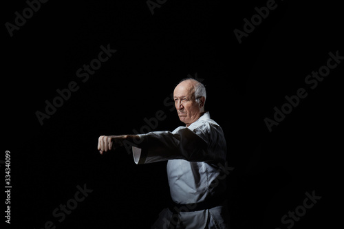 Old male athlete beats a punch with a hand on a black background