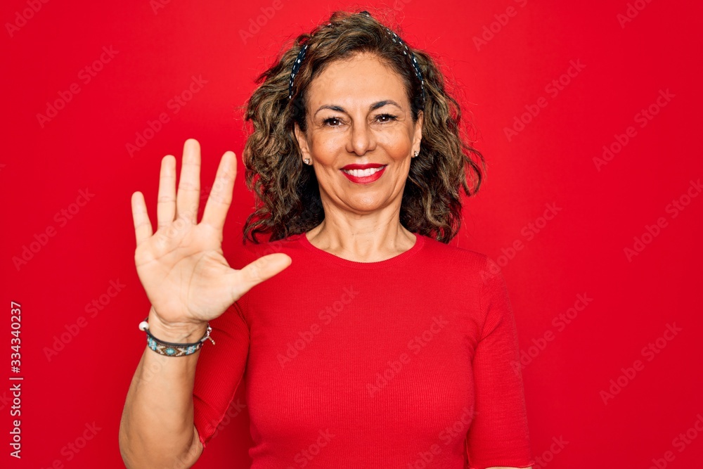 Middle age senior brunette woman wearing casual t-shirt standing over red background showing and pointing up with fingers number five while smiling confident and happy. Middle age senior brunette woman wearing casual t-shirt standing over red background showing and pointing up with fingers number five while smiling confident and happy.
