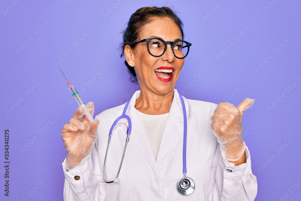 Middle age senior professional doctor woman holding syringe with medical vaccine pointing and showing with thumb up to the side with happy face smiling Middle age senior professional doctor woman holding syringe with medical vaccine pointing and showing with thumb up to the side with happy face smiling