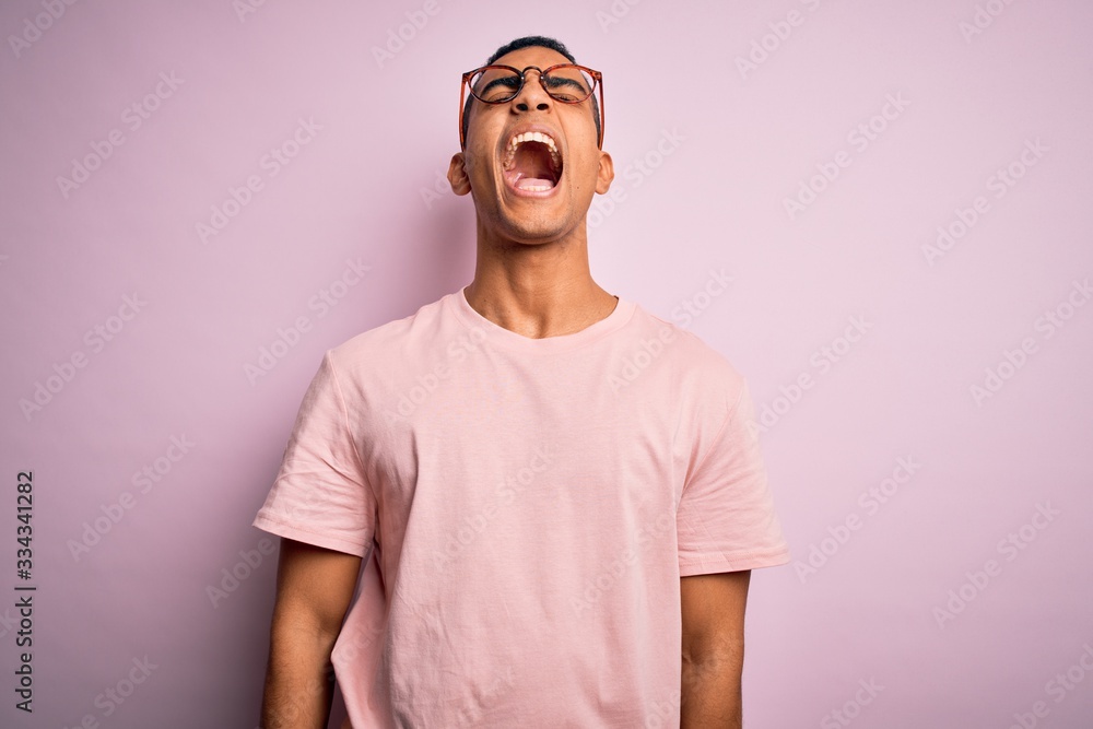 Handsome african american man wearing casual t-shirt and glasses over pink background angry and mad screaming frustrated and furious, shouting with anger. Rage and aggressive concept. Handsome african american man wearing casual t-shirt and glasses over pink background angry and mad screaming frustrated and furious, shouting with anger. Rage and aggressive concept.