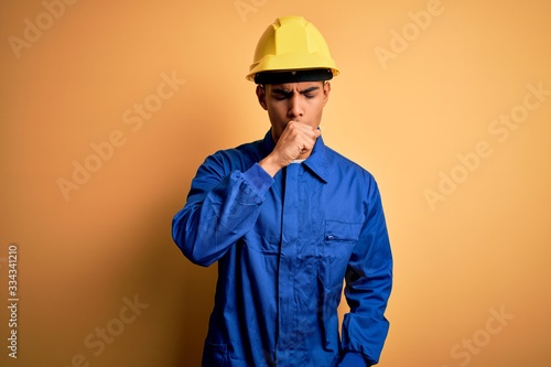 Young handsome african american worker man wearing blue uniform and security helmet feeling unwell and coughing as symptom for cold or bronchitis. Health care concept.