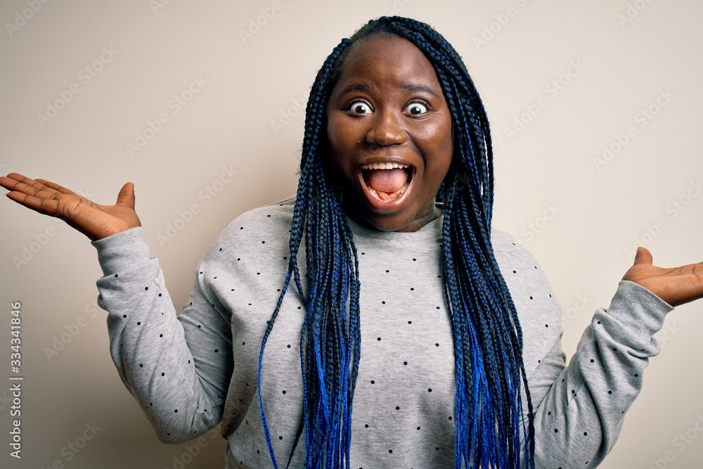 African american plus size woman with braids wearing casual sweatshirt over white background celebrating crazy and amazed for success with arms raised and open eyes screaming excited. Winner concept African american plus size woman with braids wearing casual sweatshirt over white background celebrating crazy and amazed for success with arms raised and open eyes screaming excited. Winner concept