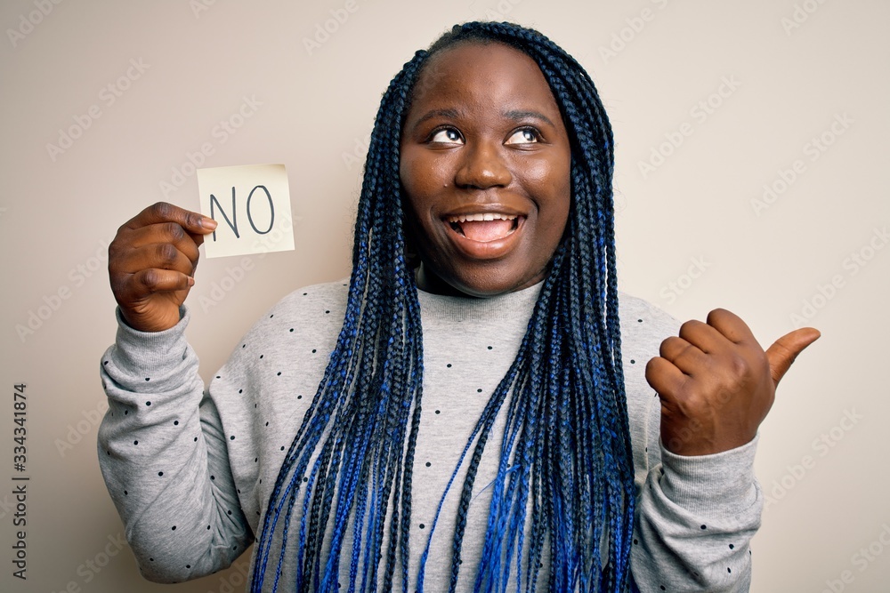 Young african american plus size woman with braids holding reminder paper with no message pointing and showing with thumb up to the side with happy face smiling Young african american plus size woman with braids holding reminder paper with no message pointing and showing with thumb up to the side with happy face smiling
