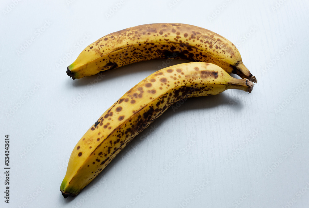 Close up to a two yellow freckled bananas in diagonal form over a white wooden table. Close up to a two yellow freckled bananas in diagonal form over a white wooden table.