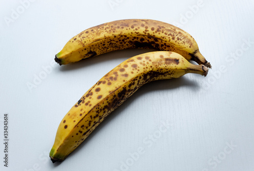 Close up to a two yellow freckled bananas in diagonal form over a white wooden table.