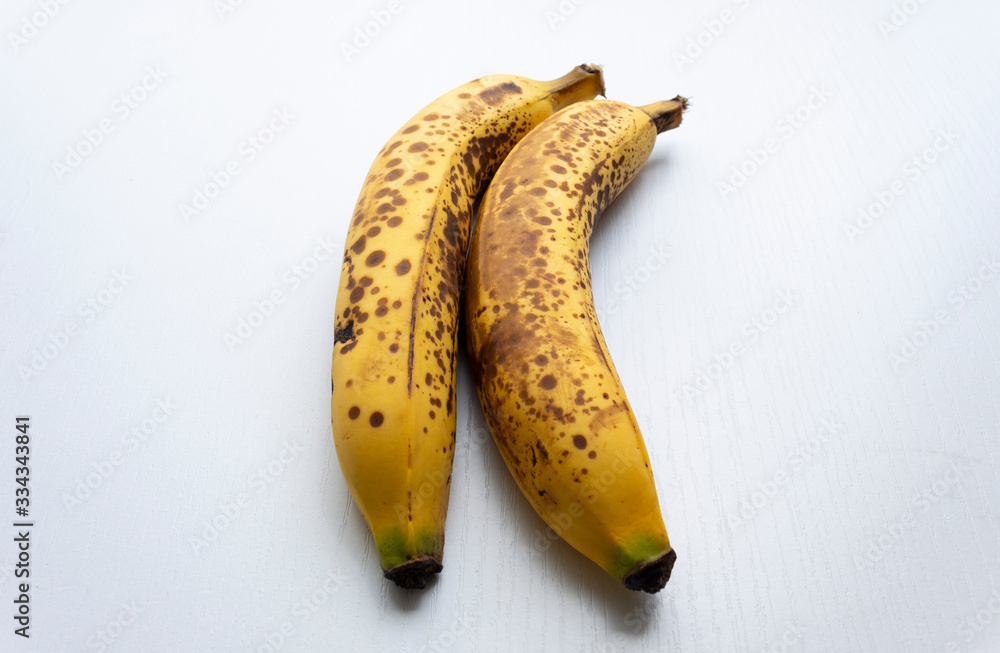 Close up to a two yellow freckled bananas in vertical form over a white wooden table. Close up to a two yellow freckled bananas in vertical form over a white wooden table.
