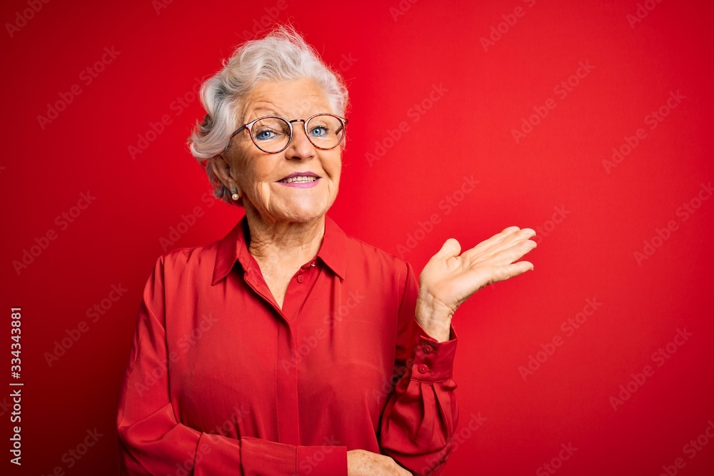 Φωτογραφία Senior beautiful grey-haired woman wearing casual shirt and glasses over red background smiling cheerful presenting and pointing with palm of hand looking at the camera