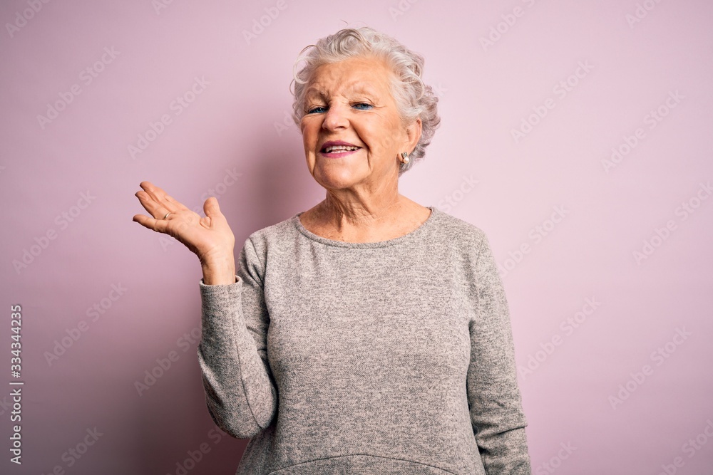 Senior beautiful woman wearing casual t-shirt standing over isolated pink background smiling cheerful presenting and pointing with palm of hand looking at the camera. Senior beautiful woman wearing casual t-shirt standing over isolated pink background smiling cheerful presenting and pointing with palm of hand looking at the camera.