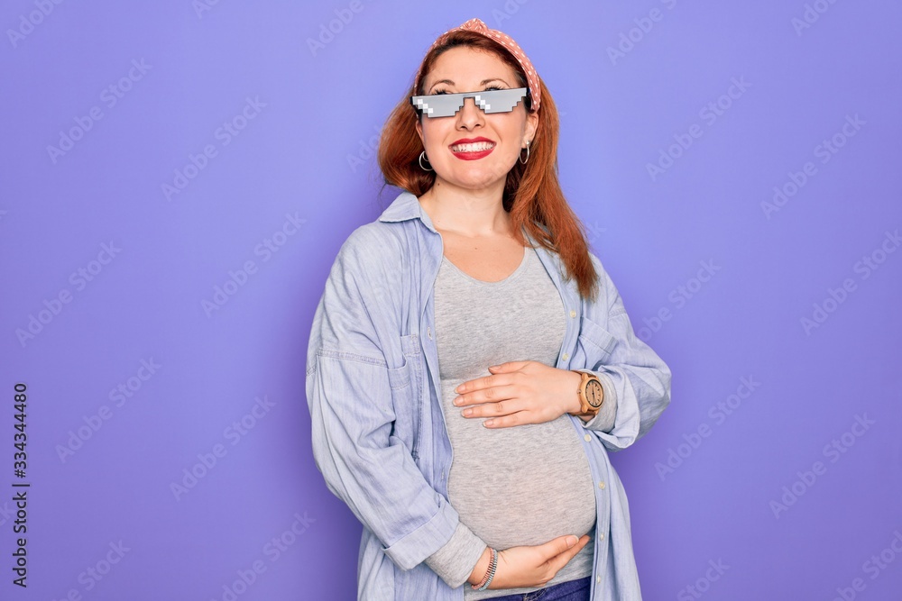 Young redhead pregnant woman expecting baby wearing funny thug life sunglasses looking away to side with smile on face, natural expression. Laughing confident. Young redhead pregnant woman expecting baby wearing funny thug life sunglasses looking away to side with smile on face, natural expression. Laughing confident.