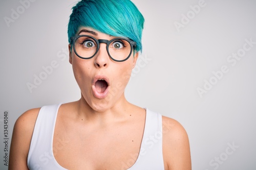 Young beautiful woman with blue fashion hair wearing casual t-shirt and glasses scared in shock with a surprise face, afraid and excited with fear expression