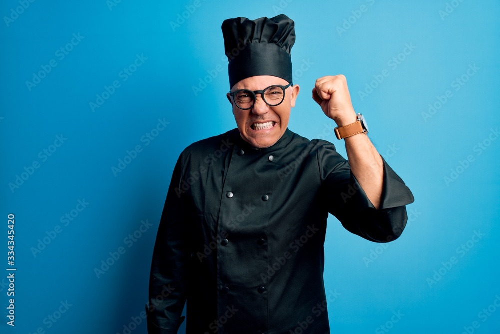 Middle age handsome grey-haired chef man wearing cooker uniform and hat angry and mad raising fist frustrated and furious while shouting with anger. Rage and aggressive concept. Middle age handsome grey-haired chef man wearing cooker uniform and hat angry and mad raising fist frustrated and furious while shouting with anger. Rage and aggressive concept.