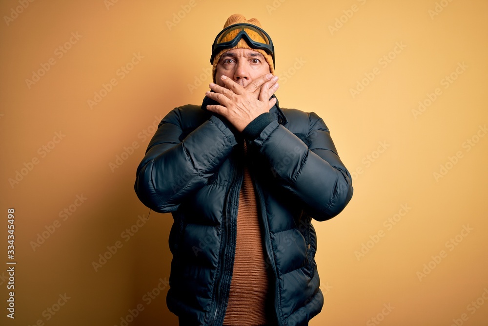 Middle age handsome grey-haired skier man on vacation wearing ski goggles shocked covering mouth with hands for mistake. Secret concept. Middle age handsome grey-haired skier man on vacation wearing ski goggles shocked covering mouth with hands for mistake. Secret concept.