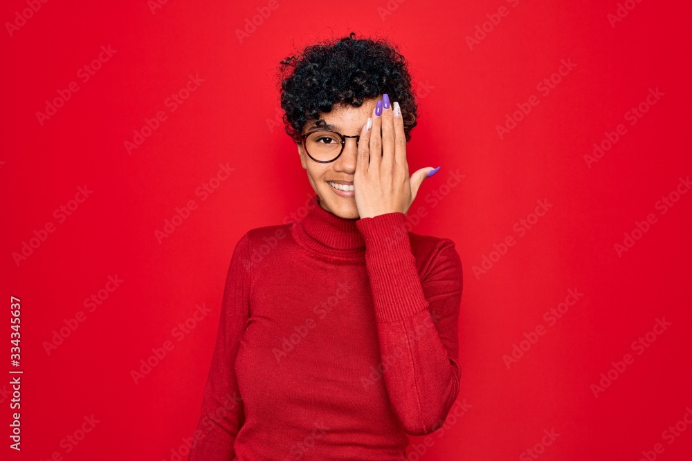 Young beautiful african american afro woman wearing turtleneck sweater and glasses covering one eye with hand, confident smile on face and surprise emotion. Young beautiful african american afro woman wearing turtleneck sweater and glasses covering one eye with hand, confident smile on face and surprise emotion.