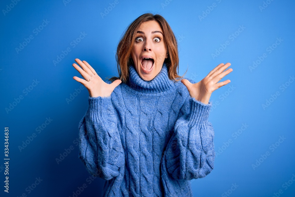 Φωτογραφία Young beautiful brunette woman wearing casual turtleneck sweater over blue background celebrating crazy and amazed for success with arms raised and open eyes screaming excited