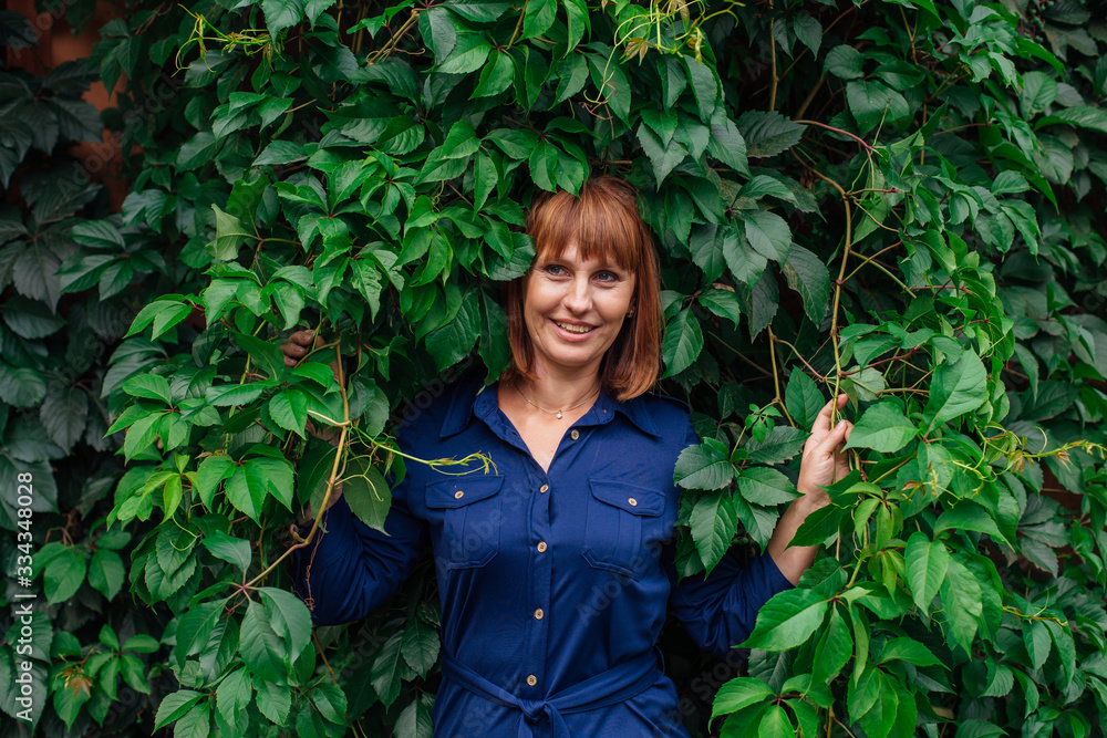 Portrait of a beautiful middle aged woman, standing next to the wall of wild grape leaves. Portrait of a beautiful middle aged woman, standing next to the wall of wild grape leaves.