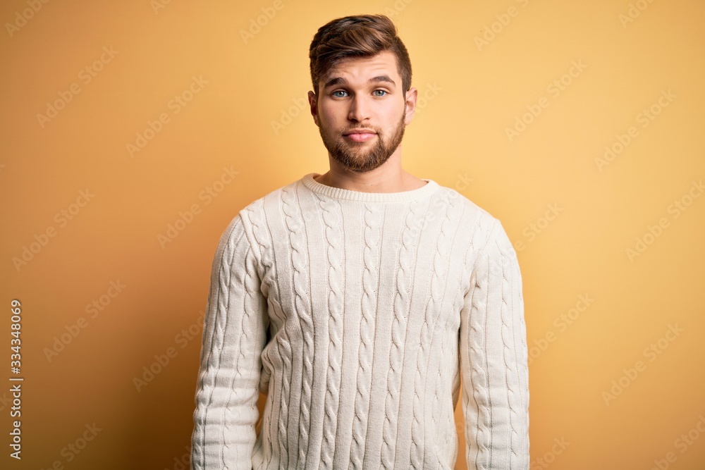 Young blond man with beard and blue eyes wearing white sweater over yellow background Relaxed with serious expression on face. Simple and natural looking at the camera. Young blond man with beard and blue eyes wearing white sweater over yellow background Relaxed with serious expression on face. Simple and natural looking at the camera.